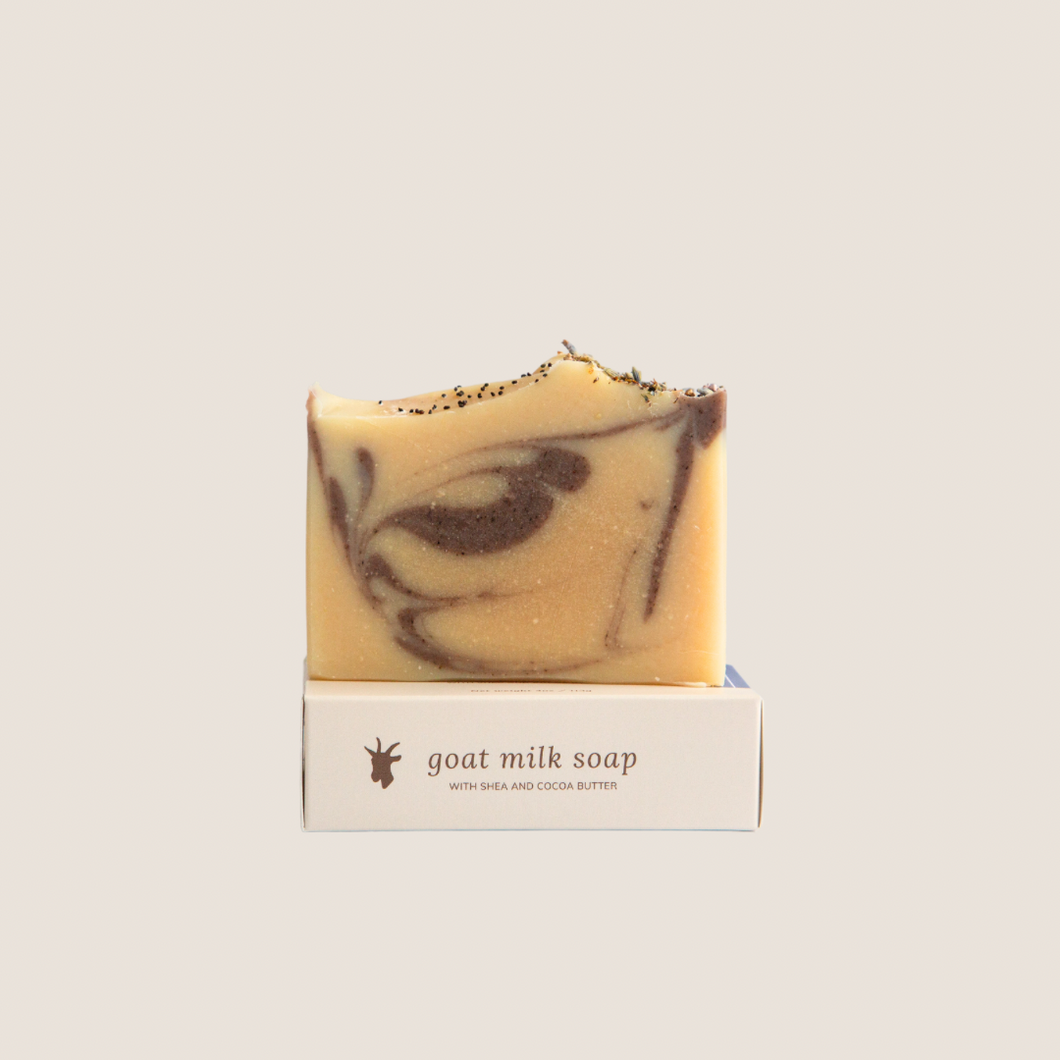 A bar of lavender clove goat milk soap on top of it's soap box