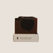 Load image into Gallery viewer, A bar of black amber and lavender goat milk soap on top of it&#39;s box with beige background
