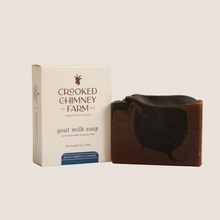 Load image into Gallery viewer, A bar of black amber and lavender goat milk soap next to it&#39;s box with beige background
