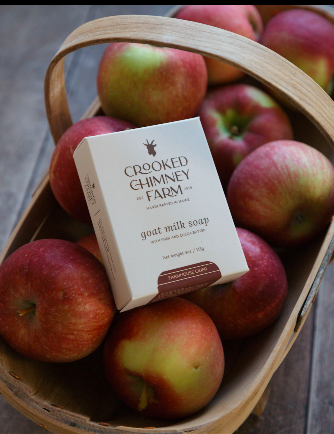 a box of crooked chimney farm farmhouse cider soap set on top of a basket of apples. 