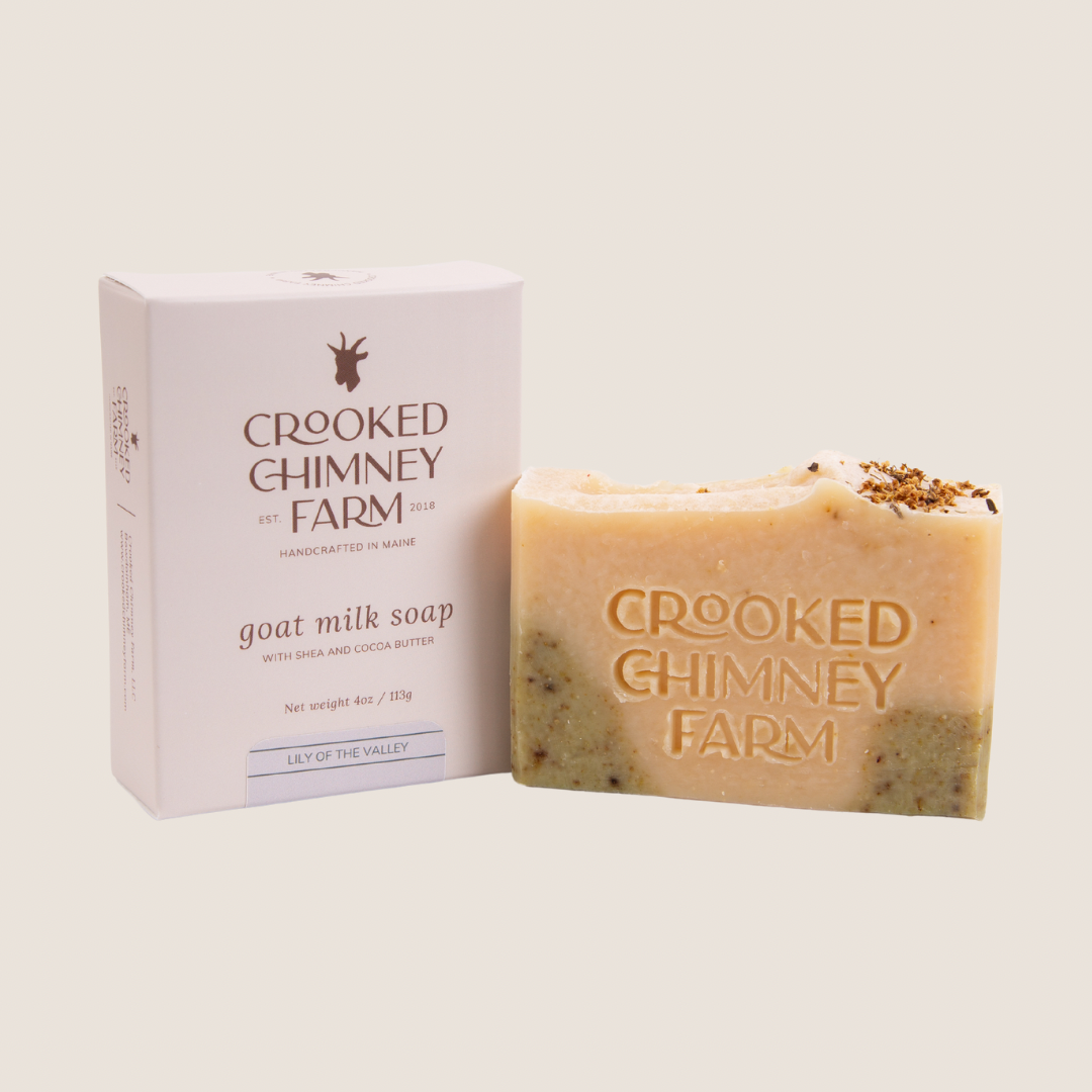 A bar of crooked chimney farm lily of the valley goat milk soap next to soap box