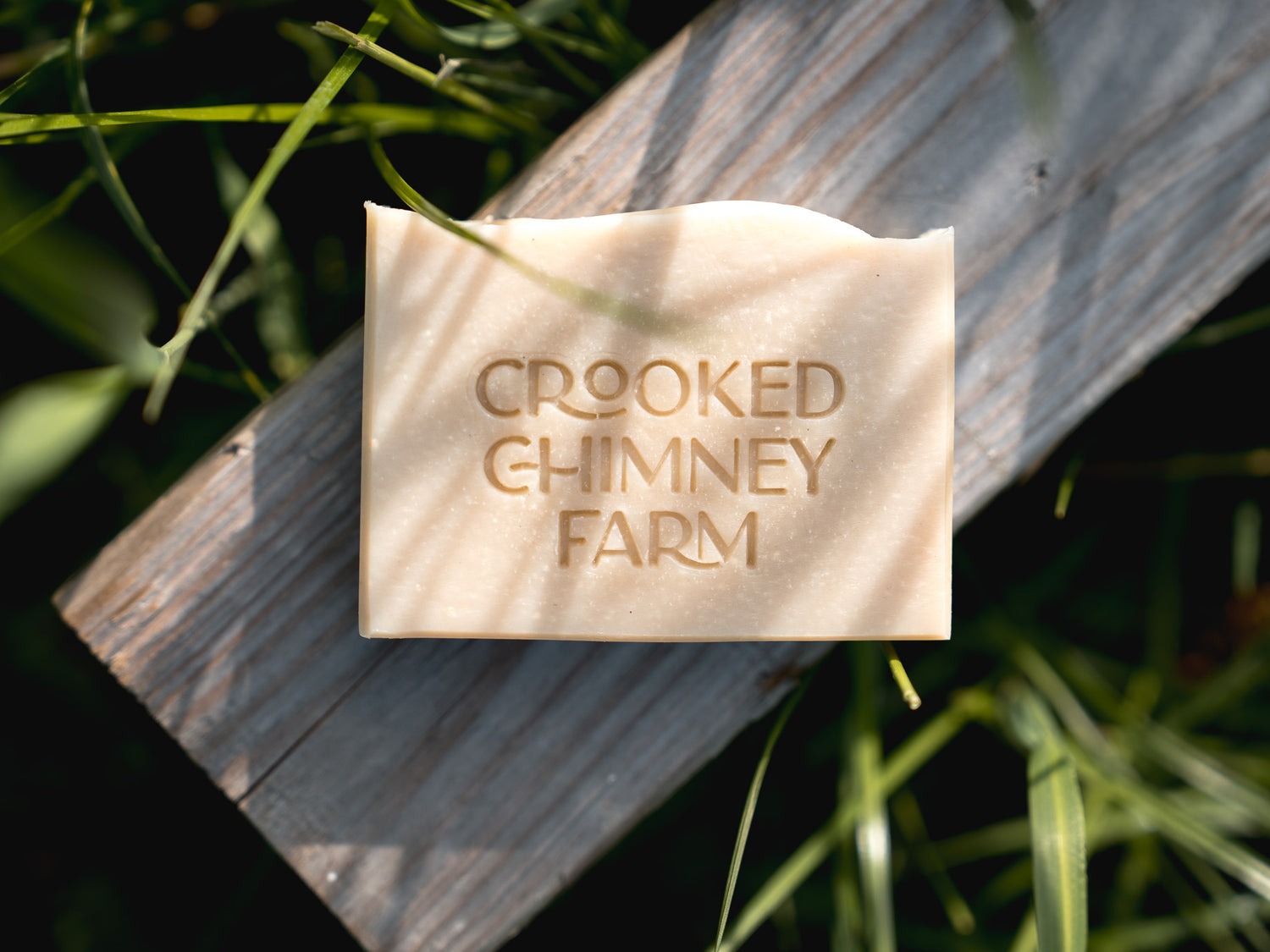 Field (fresh basil and verbena) goat milk soap on a weathered board with grass in the background.