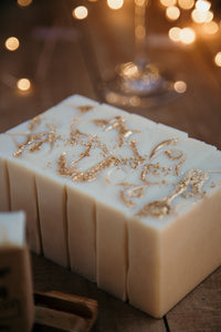 a loaf of champagne problems soap cut into bars with a champagne glass and twinkle lights in the background.