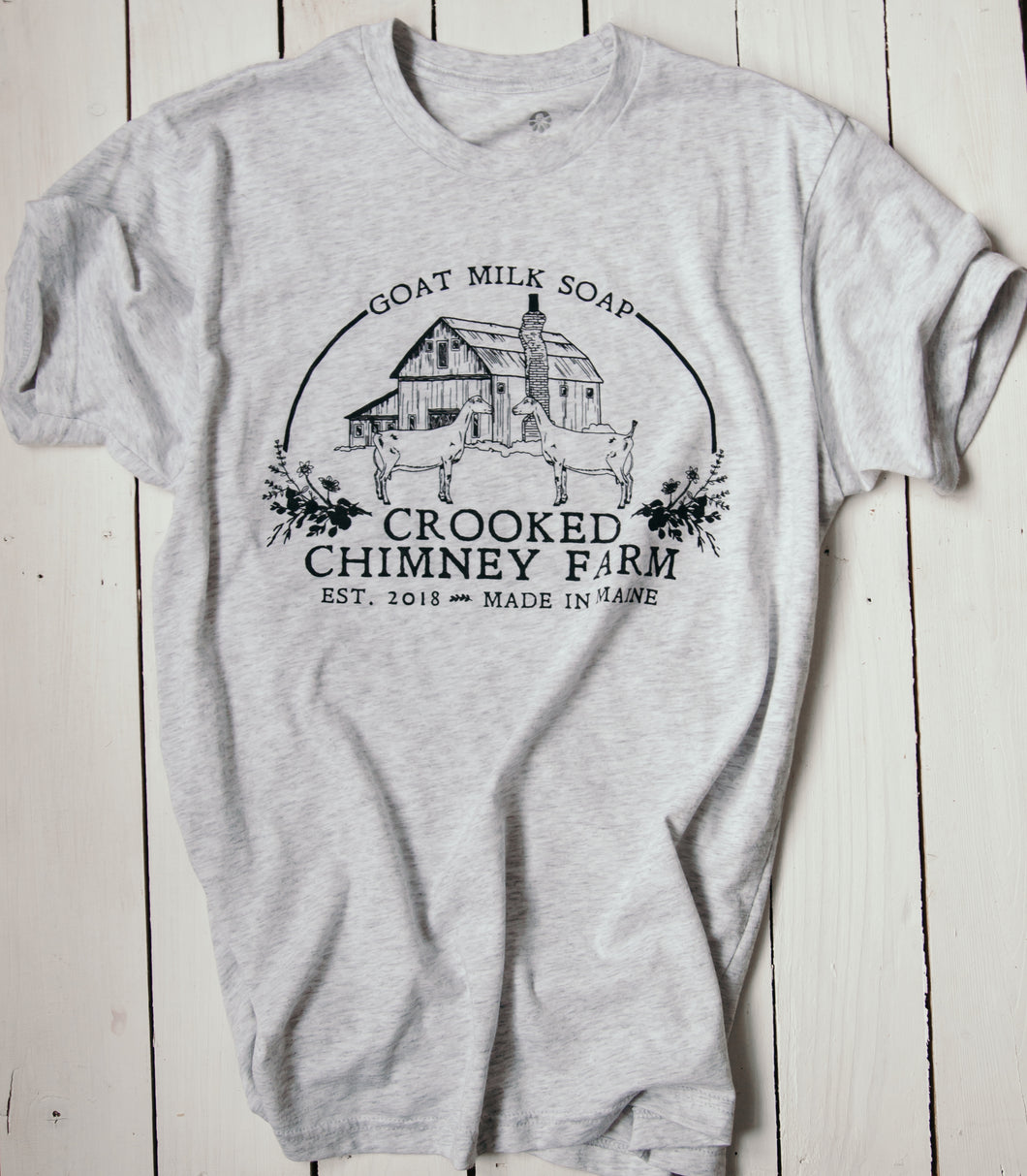 Heathered white tee shirt with Crooked Chimney Farm logo on the front center. Logo has 2 goats and a barn. 