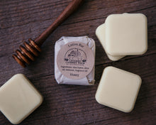 Load image into Gallery viewer, honey solid lotion bar wrapped in tissue paper with ingredient label. Surrounded by unwrapped lotion bars and honey drizzle stick.
